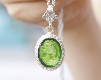 Puede incluir: Un collar de cadena de plata con un colgante de camafeo verde que presenta el perfil de una mujer. El colgante está engastado en un marco de plata con un diseño de cuerda.