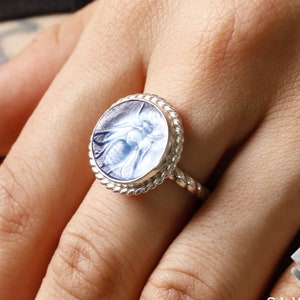 May include: A silver ring with a blue glass bee cameo. The ring has a rope-like band and a round bezel.