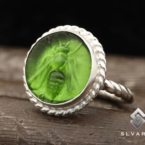 May include: A silver ring with a green glass cameo featuring a detailed bee design.