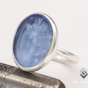 May include: A silver ring with a blue cameo featuring a woman's profile and a floral design.
