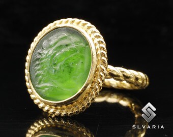 May include: A gold ring with a green glass cameo featuring a carved profile. The ring band is twisted and has a rope-like design.