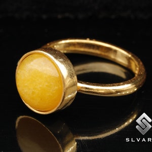 Puede incluir: Un anillo de oro con una gran piedra preciosa redonda y amarilla. El anillo es simple y elegante.