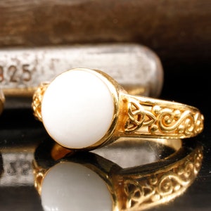 Puede incluir: Un anillo de oro con una piedra ovalada blanca y un diseño de nudo celta.