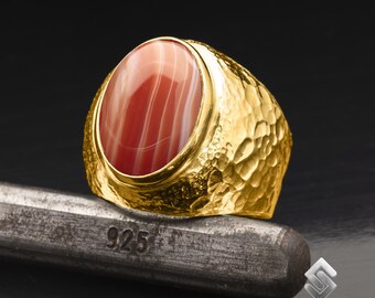May include: A gold ring featuring a red and white agate gemstone. The ring has a hammered texture and is marked "925" on the band.
