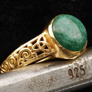 Puede incluir: Un anillo de oro con una piedra preciosa verde y un diseño de nudo celta. El anillo está marcado con 925, lo que indica que está hecho de plata de ley.