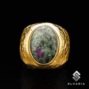 May include: A gold ring featuring a green and pink oval gemstone set in a textured band.