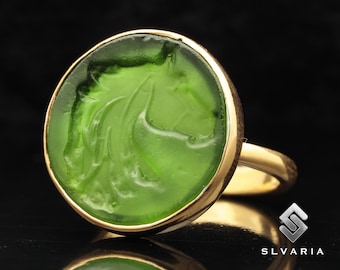May include: A gold ring with a green glass cameo featuring a horse's head in profile.