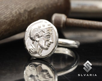 May include: A silver ring with a detailed design of a woman's face on the top. The ring is made of a smooth, polished metal.