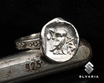 May include: A silver ring with a detailed design of a bird on the top. The ring is sitting on a metal surface with the number 925 stamped on it.