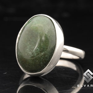 Op de afbeelding: Een zilveren ring met een groene ovale edelsteen. De ring heeft een gladde, gepolijste afwerking en een eenvoudig ontwerp.