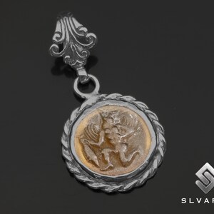 Könnte beinhalten: Silberner Anhänger mit einem runden, goldfarbenen Kamee, der ein detailliertes Bild einer mythologischen Figur zeigt. Der Anhänger hat eine dekorative Öse.