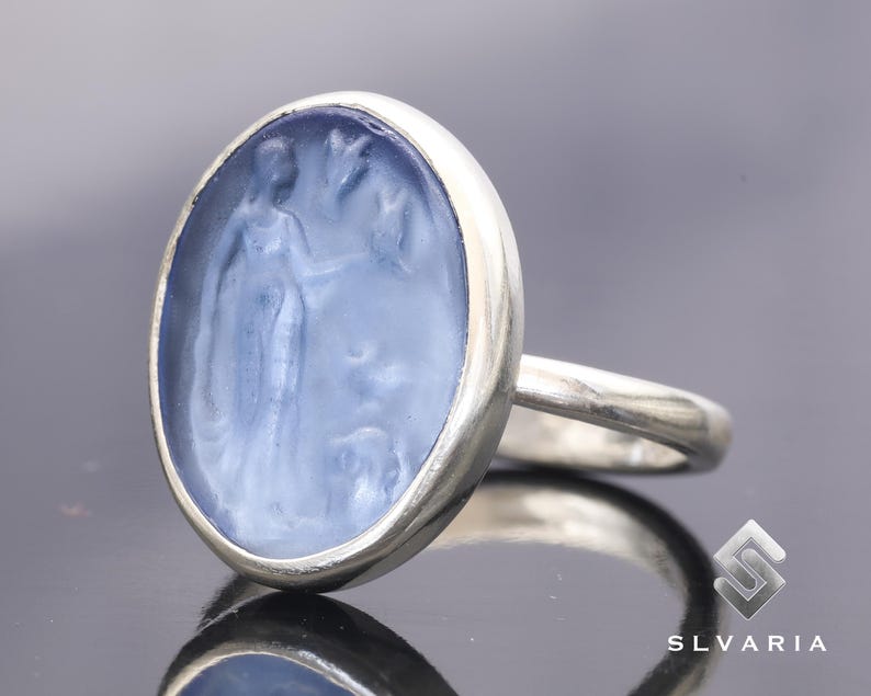 May include: A silver ring with a blue cameo featuring a carved image of a woman. The cameo is set in a silver oval bezel.