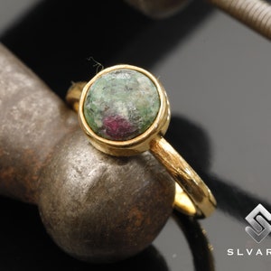 Peut inclure: Une bague en or avec une pierre précieuse verte et rose. La bague a une bande texturée.