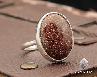 May include: A silver ring with a large oval-shaped brown gemstone. The gemstone has a sparkly, glittery texture.