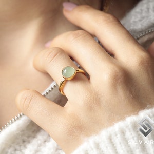 May include: A gold ring with a light green gemstone. The ring is on a person's finger.