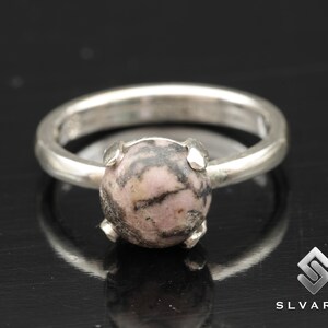 May include: A silver ring with a pink and black gemstone set in a prong setting.