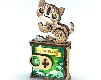 May include: A wooden cat figurine with a spotted pattern sits atop a box featuring the word "TAIWAN" on a banner. The box has a green background with animal silhouettes and a controller design.