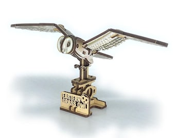May include: A wooden Eastern Grass Owl model with outstretched wings. The owl is light brown with darker brown wing edges and a detailed, textured wing design. The base features the text "Eastern Grass Owl".