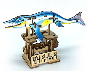 May include: A wooden puzzle of a Tylosaurus proriger, a prehistoric marine reptile. The puzzle is blue, yellow, and white, with a detailed design. The base of the puzzle has the text "TYLOSAURUS PRORIGER".