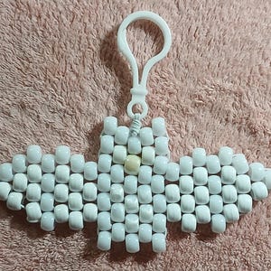 White aethetic Kandi Bat with semiopaque body and opaque wings, pearly white belly, opal like nose, and opaque off-white eyes, done on white stretchy cord and finished with a matching white hook.