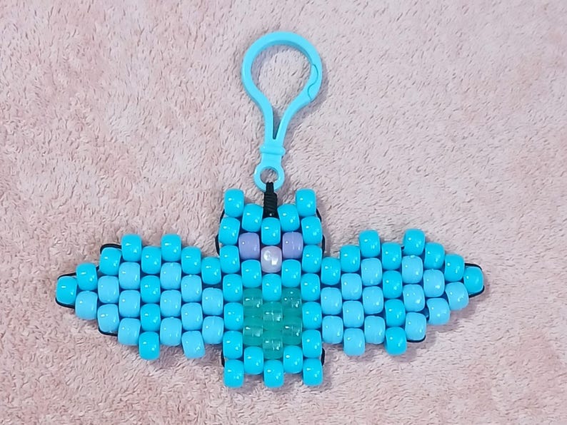 Light blue aethetic Kandi Bat with a light blue body, pastel blue wings, UV reactive transparent light blue belly, light pearly pink nose, and lavendar eyes, done on black stretchy cord and finished with a light blue hook.