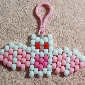 Coquette aethetic Kandi Bat with a white body and light pink wings, pink belly, UV reactive transparent light pink nose, and red eyes, done on white stretchy cord and finished with a matching light pink hook.