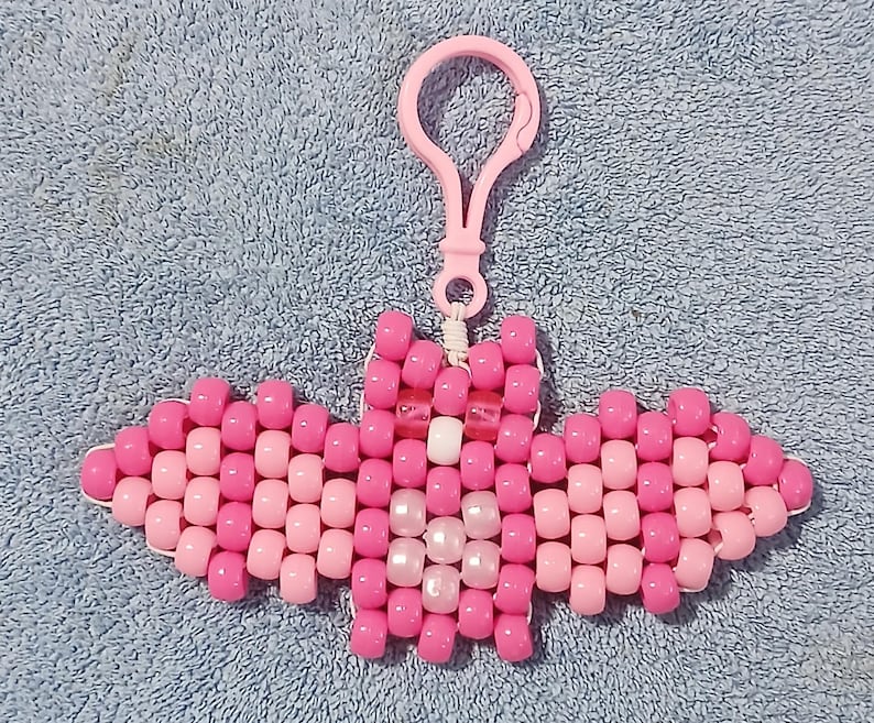 Valentines Pink aethetic Kandi Bat with a pink body, light pink wings, pearly light pink belly, white nose, UV reactive pink eyes, and done on white stretchy cord finished with a light pink hook.