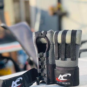 Könnte beinhalten: Ein Paar schwarze und graue fingerlose Handschuhe mit einem Netzdesign und einem schwarzen Band mit dem Logo "AC Aces Sports".