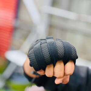 K&ouml;nnte beinhalten: Nahaufnahme einer Hand, die schwarze gepolsterte Handschuhe tr&auml;gt, mit den Fingern zu einer Faust geballt.