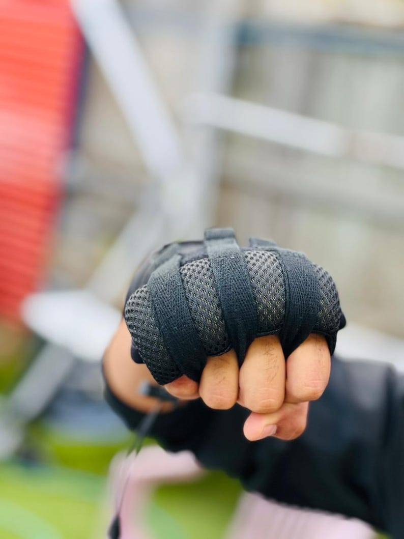 K&ouml;nnte beinhalten: Nahaufnahme einer Hand, die schwarze gepolsterte Handschuhe tr&auml;gt, mit den Fingern zu einer Faust geballt.