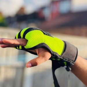 Op de afbeelding: Close-up van een zwarte en neon groene trainingshandschoen met een band. De handschoen heeft een mesh-ontwerp en is vingerloos.