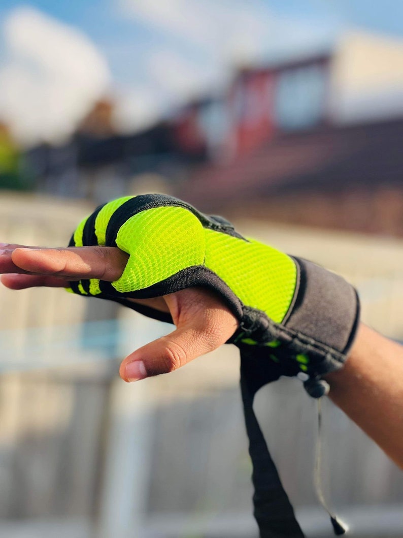 Op de afbeelding: Close-up van een zwarte en neon groene trainingshandschoen met een band. De handschoen heeft een mesh-ontwerp en is vingerloos.