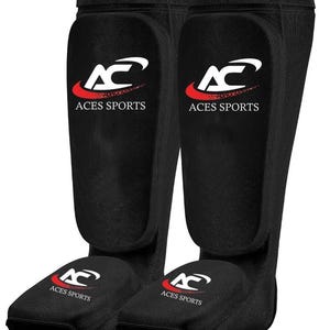 May include: Pair of black shin guards with the "ACES SPORTS" logo in white and red. The guards are designed to protect the shins and feet. The logo features a stylized "AC" with a swoosh.