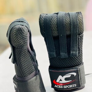 K&ouml;nnte beinhalten: Ein Paar schwarze fingerlose Trainingshandschuhe mit atmungsaktivem Mesh-Design und verstellbaren Handgelenksriemen. Die Handschuhe haben das Logo "AC Aces Sports" auf dem Handgelenksriemen.