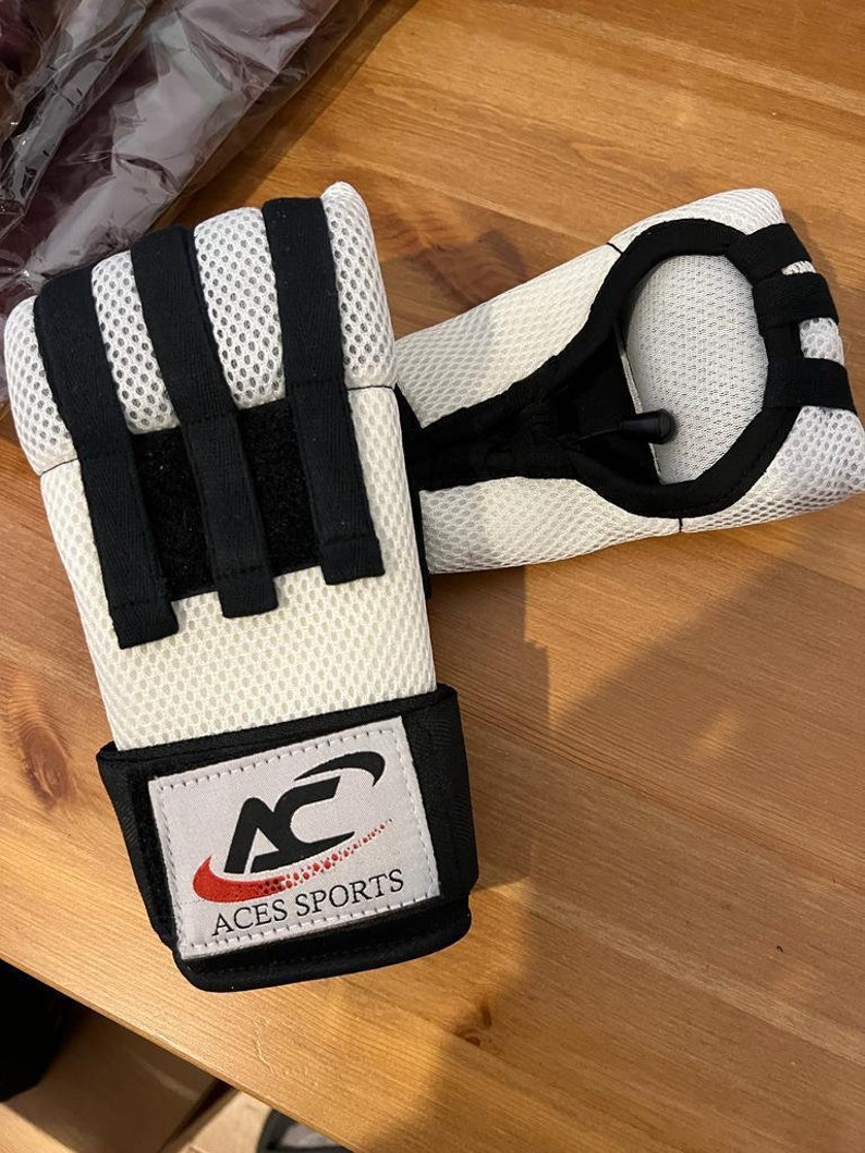 May include: A pair of white and black boxing hand wraps with a black strap and the logo "ACES SPORTS" in red and white.