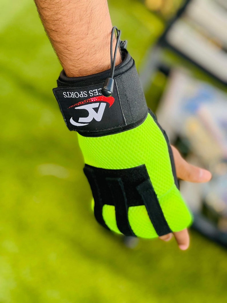 Op de afbeelding: Groene en zwarte gewichthefgloves met een polsband. De band heeft de tekst "AC" en "CES SPORTS" in rood.