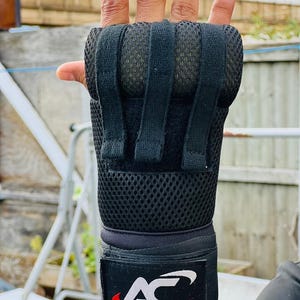 K&ouml;nnte beinhalten: Schwarze Handgelenksbandagen mit einem Mesh-Panel und einem Klettverschluss. Die Bandagen haben einen gepolsterten Bereich zum Schutz. Das Markenlogo ist "Aces Sports" in wei&szlig;er Schrift auf schwarzem Hintergrund mit einem roten Schwung.