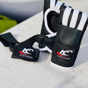 Könnte beinhalten: Ein Paar schwarze Handgelenkschützer mit weißen Streifen und einem roten Logo mit der Aufschrift "Aces Sports".