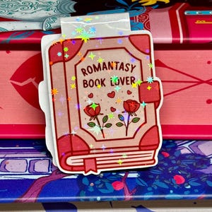 May include: A pink and red book-shaped bookmark with glitter and the text "Romantasy Book Lover". The bookmark features two red roses with green stems and leaves.