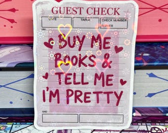 May include: A guest check-shaped holographic sticker with the text "BUY ME BOOKS & TELL ME I'M PRETTY" in red, decorated with hearts and stars. The background shows a stack of books in various colours.