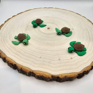 May include: Four small green and brown turtle figurines on a wooden surface. The turtles have black eyes and are facing different directions.