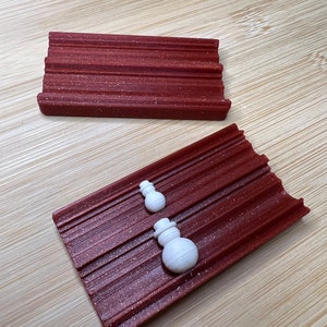 Könnte beinhalten: Zwei weiße Schneemann-förmige Ornamente auf einer roten, strukturierten, rechteckigen Schale. Die Schale hat eine geriffelte Oberfläche.