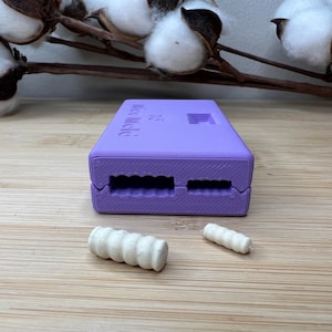 Könnte beinhalten: Eine violette Plastikform mit dem Text "Mini Macarons" auf der Oberseite. Zwei weiße Makronenschalen liegen auf einer Holzoberfläche.