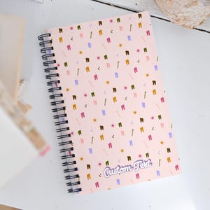 May include: A pink spiral notebook with a colourful tooth and toothbrush pattern. The notebook has the text "Custom Text" printed on the front cover.