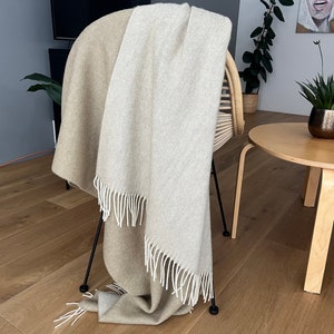 May include: A beige and white throw blanket with fringe on a black chair. The blanket is draped over the back of the chair and is hanging down the sides.