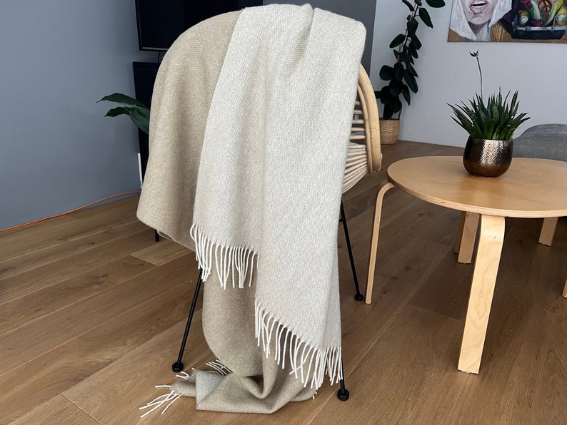 May include: A beige and white throw blanket with fringe on a black chair. The blanket is draped over the back of the chair and is hanging down the sides.