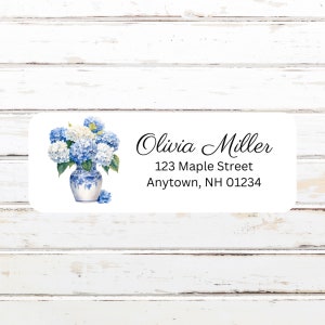 May include: A white label with a blue and white floral illustration of hydrangeas in a vase. The text on the label reads "Olivia Miller, 123 Maple Street, Anytown, NH 01234".