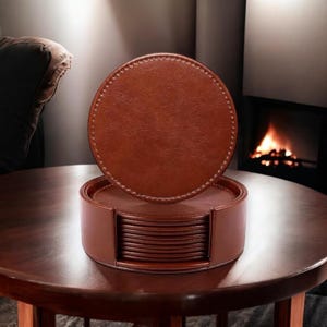 May include: A set of brown leather coasters with stitched edges, stacked in a round holder. The coasters are made of faux leather and have a smooth, polished finish.