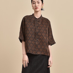 May include: A woman is wearing a brown and black patterned short-sleeved shirt with a black skirt and black slip-on shoes.