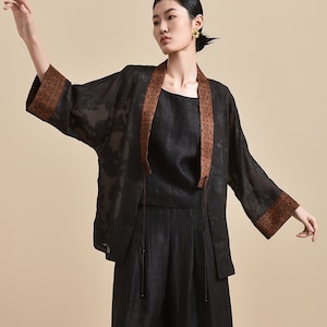 Puede incluir: Un kimono negro de gasa transparente con bordados florales marrones y un top de lino negro a juego y pantalones anchos. La modelo lleva mules de cuero negro.